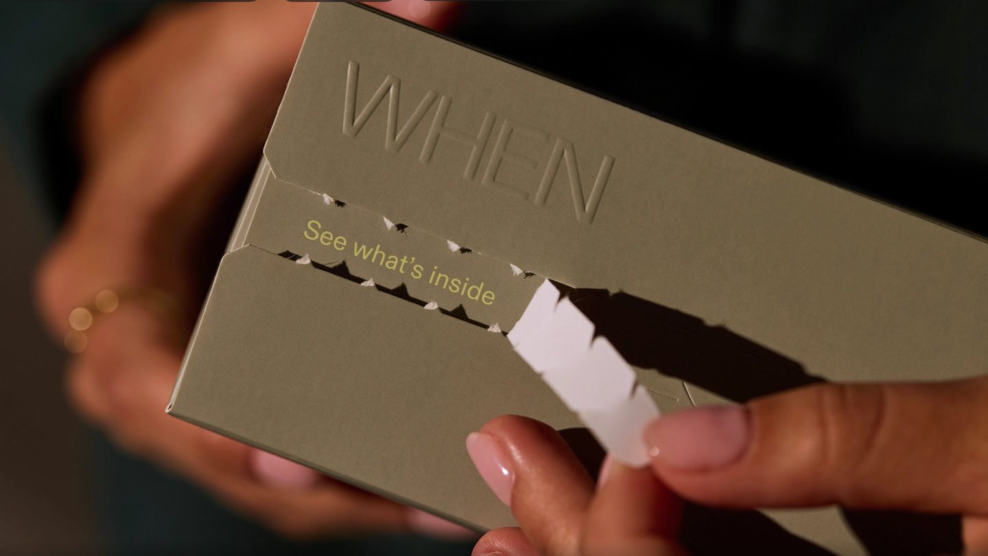 Hands opening a kraft box embossed with the word WHEN